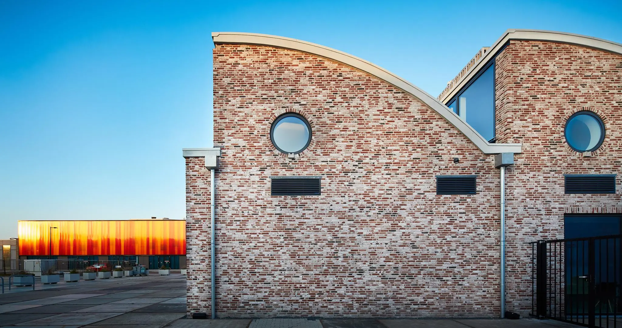 Bakstenen gebouw aan de Abram Dudok van Heelstraat met ronde ramen en gebogen daklijnen, bij zonsondergang.