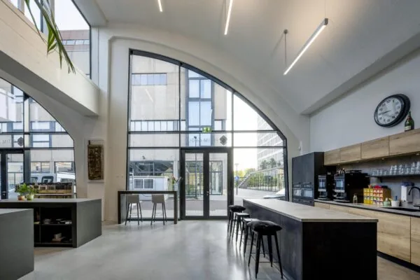 Moderne open kantoorruimte aan de Abram Dudok van Heelstraat met hoge ramen, een koffiehoek en een zithoek.