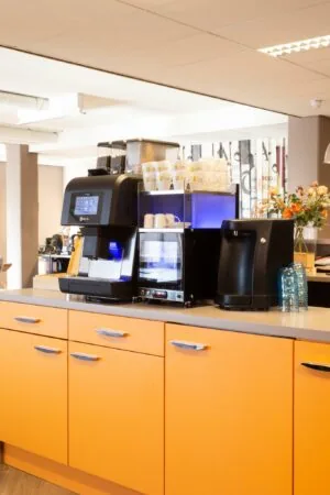 Koffiecorner met moderne koffiemachine, kopjes en oranje keukenkastjes aan de Zaagmolenlaan.