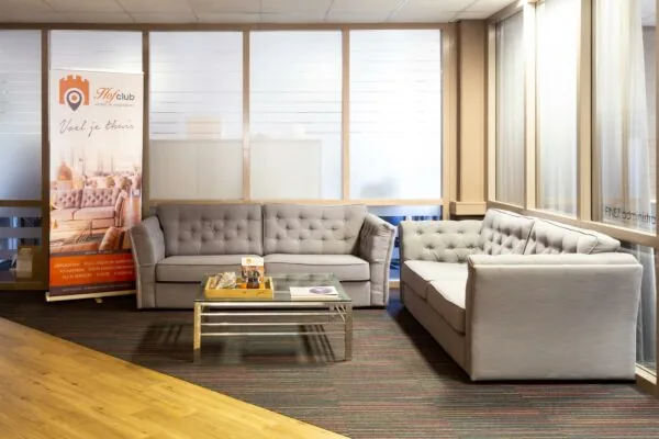 Zitruimte met grijze banken en een glazen salontafel in de wachtruimte van Hofclub Zaagmolenlaan.