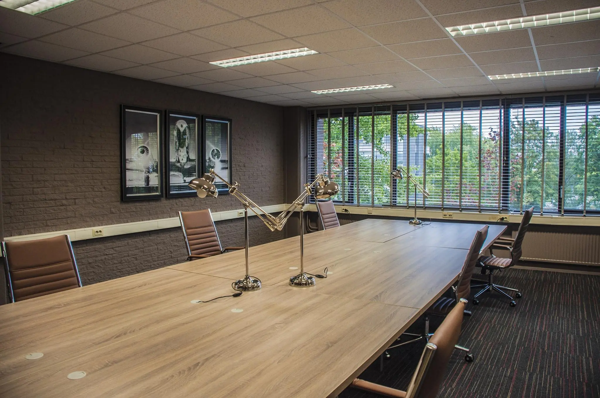 Vergaderruimte aan de Zaagmolenlaan met een lange houten tafel, lederen stoelen, bureaulampen en grote ramen met jaloezieën.