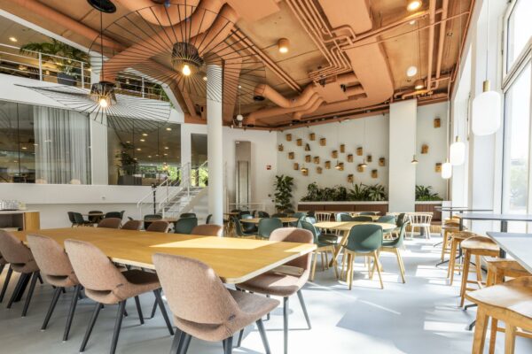 Moderne en lichte kantine in een kantoor aan de Bezuidenhoutseweg met houten tafels, designstoelen en groene accenten.