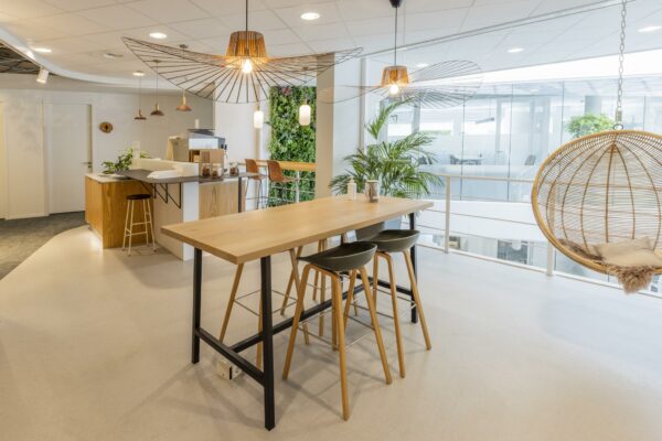 Moderne kantoorruimte aan de Bezuidenhoutseweg met een open keuken, hoge tafels, hangstoel en veel natuurlijke elementen.