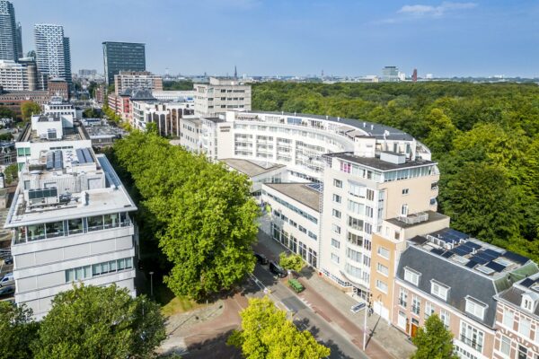 Luchtfoto van de Bezuidenhoutseweg in Den Haag met moderne en historische gebouwen langs een groene laan.