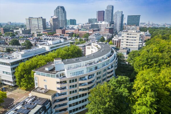 Luchtfoto van het iconische ronde appartementencomplex aan de Bezuidenhoutseweg in Den Haag met de skyline van de stad op de achtergrond.