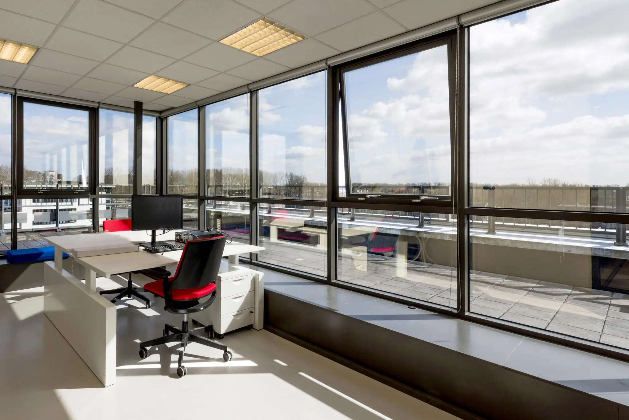 Modern hoekkantoor aan de Anthony Fokkerweg met grote ramen, een bureauopstelling en uitzicht op een ruim dakterras.