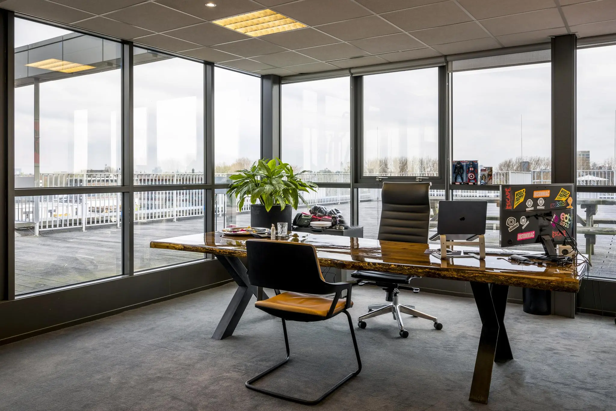 Modern kantoor met glazen wanden, een houten bureau en uitzicht op een dakterras aan de Anthony Fokkerweg.