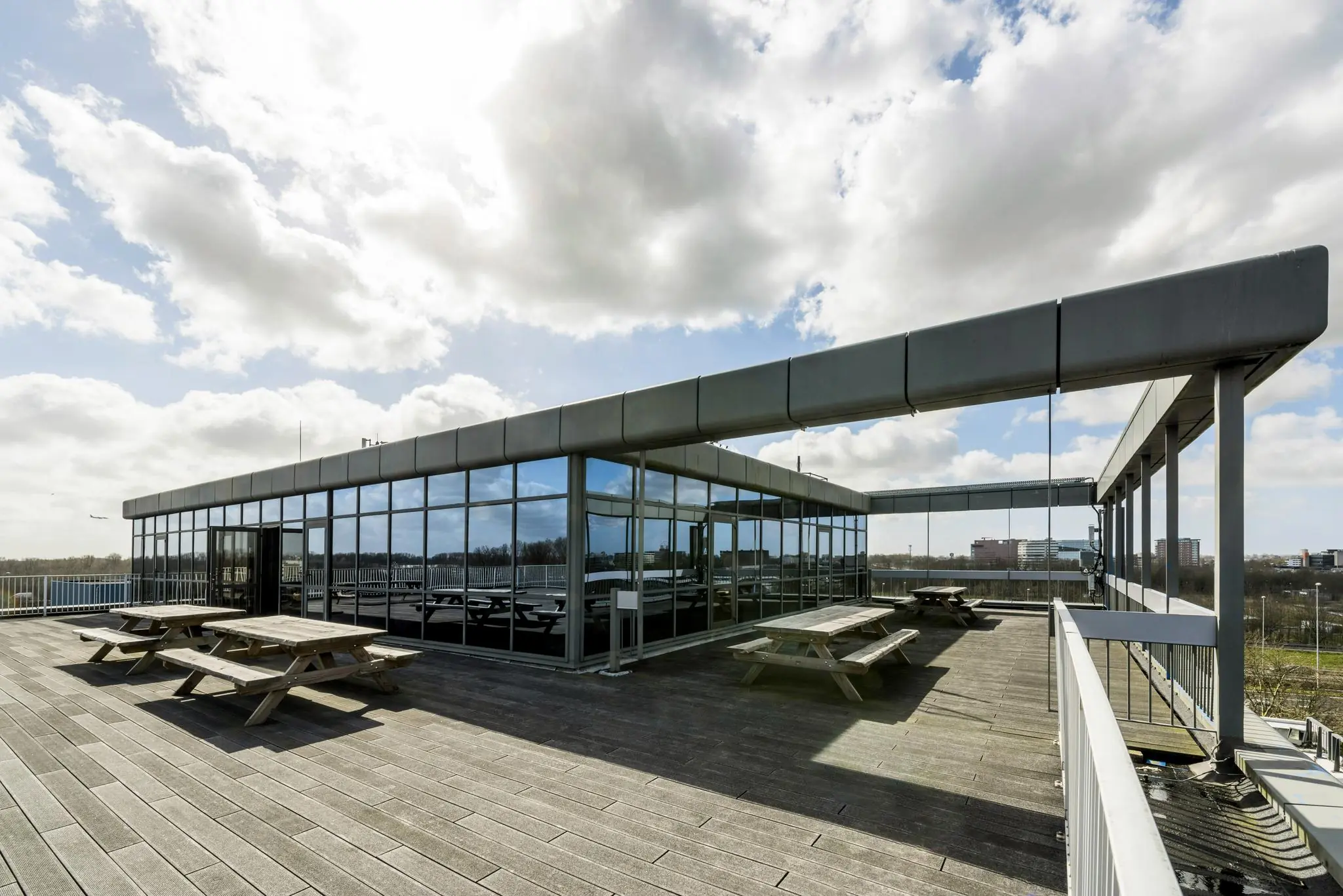 Dakterras met picknicktafels en glazen gevel aan de Anthony Fokkerweg, onder een deels bewolkte hemel.