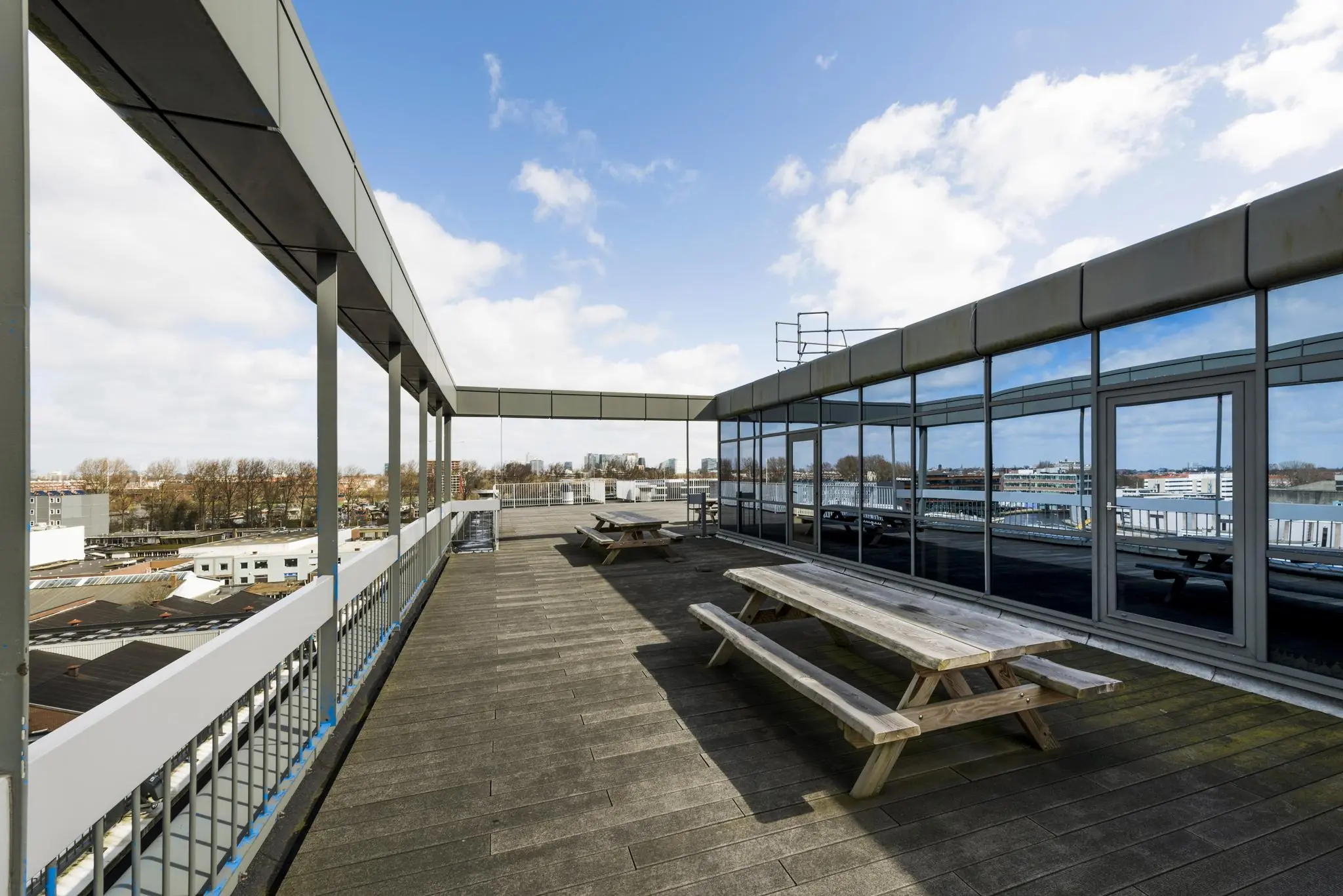Dakterras met houten picknicktafels bij een kantoorgebouw aan de Anthony Fokkerweg, met uitzicht over een industriegebied.