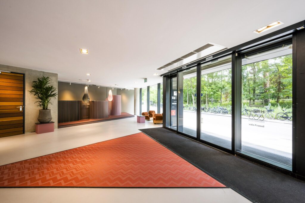 Moderne entreehal aan de Generaal Vetterstraat met grote glazen schuifdeuren, stijlvolle inrichting en uitzicht op fietsen buiten.