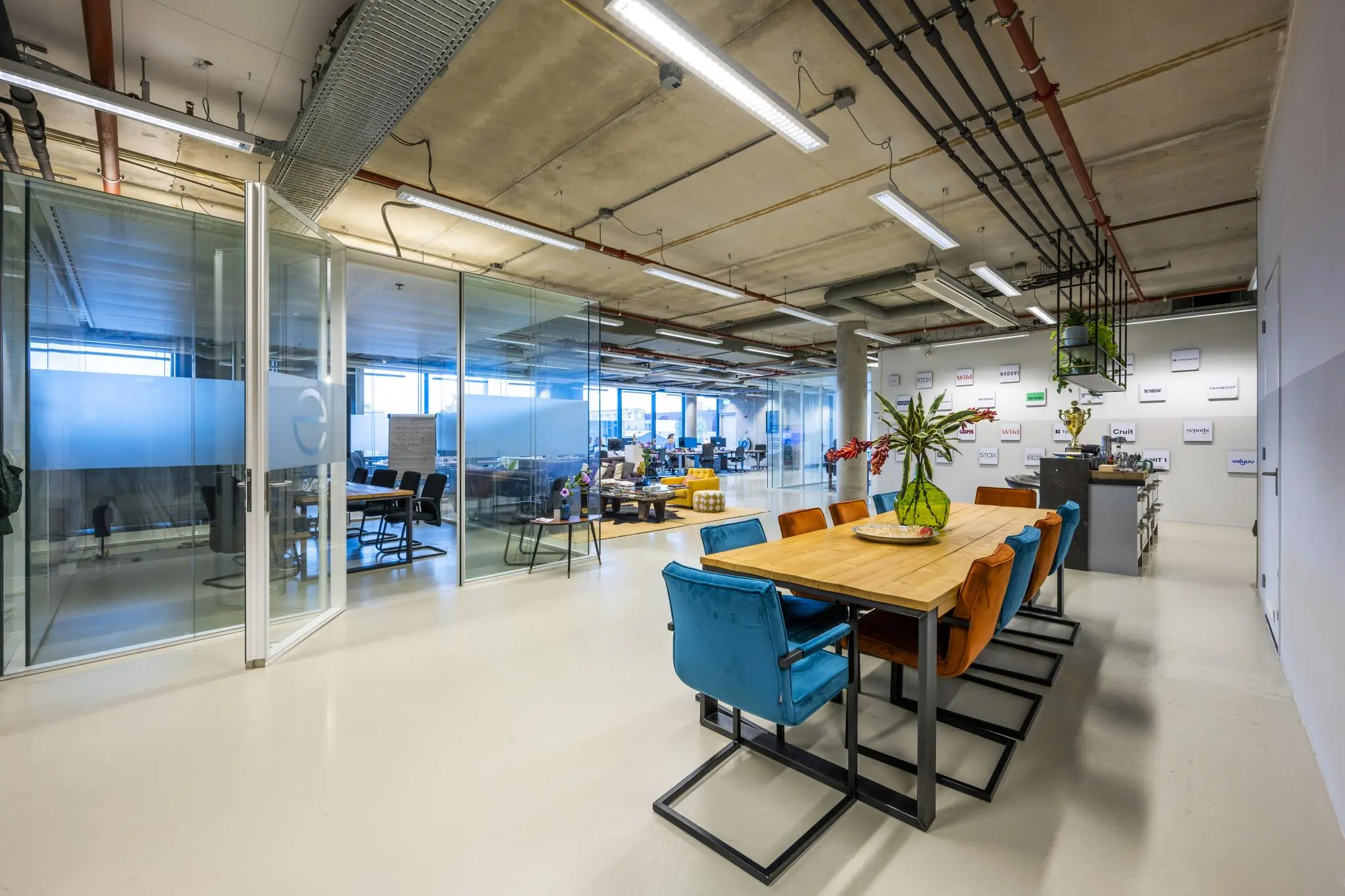 Moderne kantoorruimte aan de Generaal Vetterstraat met glazen vergaderruimtes, open werkplekken en een houten vergadertafel met kleurrijke stoelen.