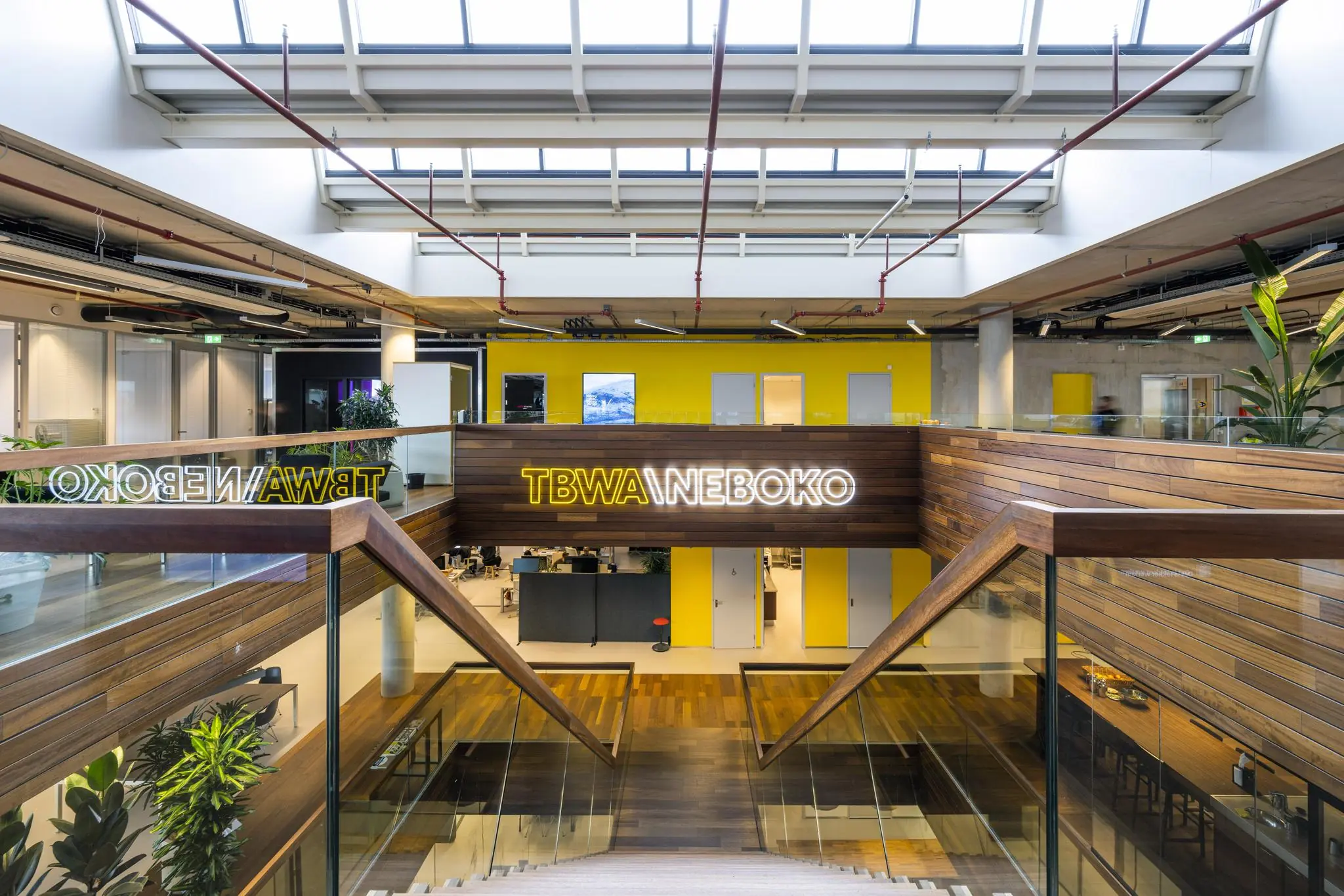 Moderne kantoorruimte van TBWANEBOKO aan de Generaal Vetterstraat met houten afwerking, glazen balustrades en een opvallende gele achterwand.