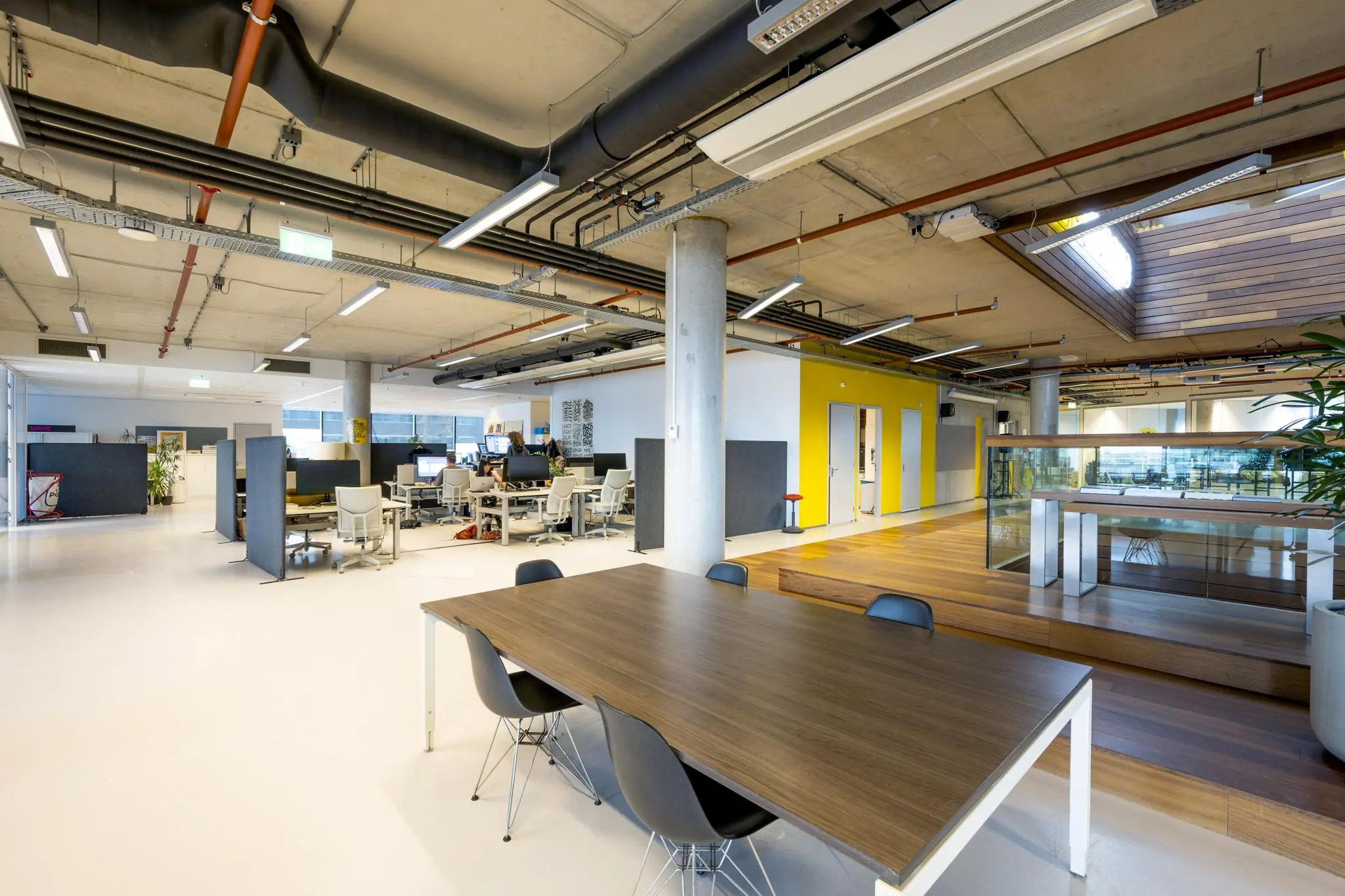 Moderne open kantoorruimte aan de Generaal Vetterstraat met werkplekken, vergadertafel en gele accentmuur.