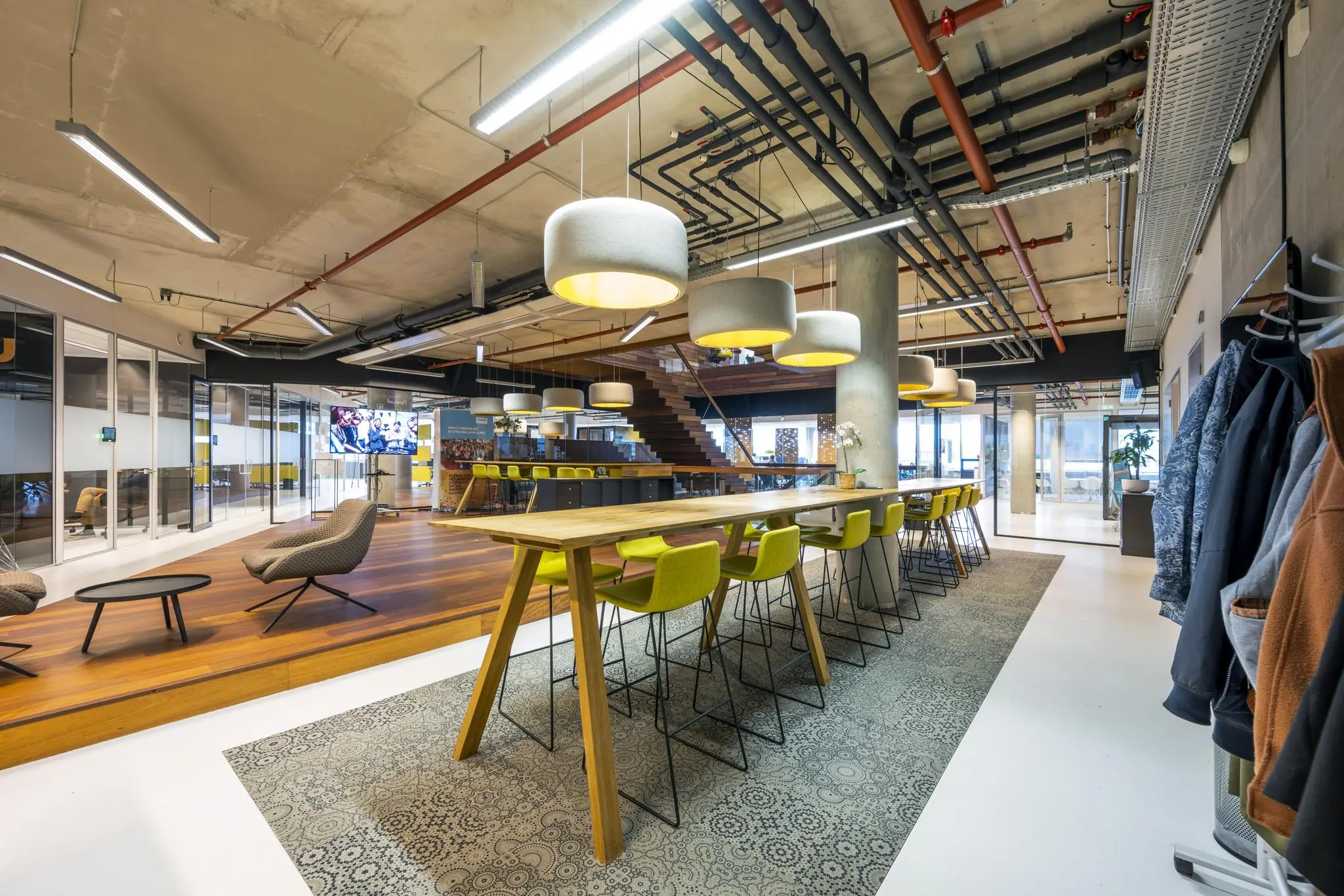 Moderne kantoorruimte aan de Generaal Vetterstraat met lange vergadertafel, gele barkrukken, loungehoek en industriële plafondafwerking.