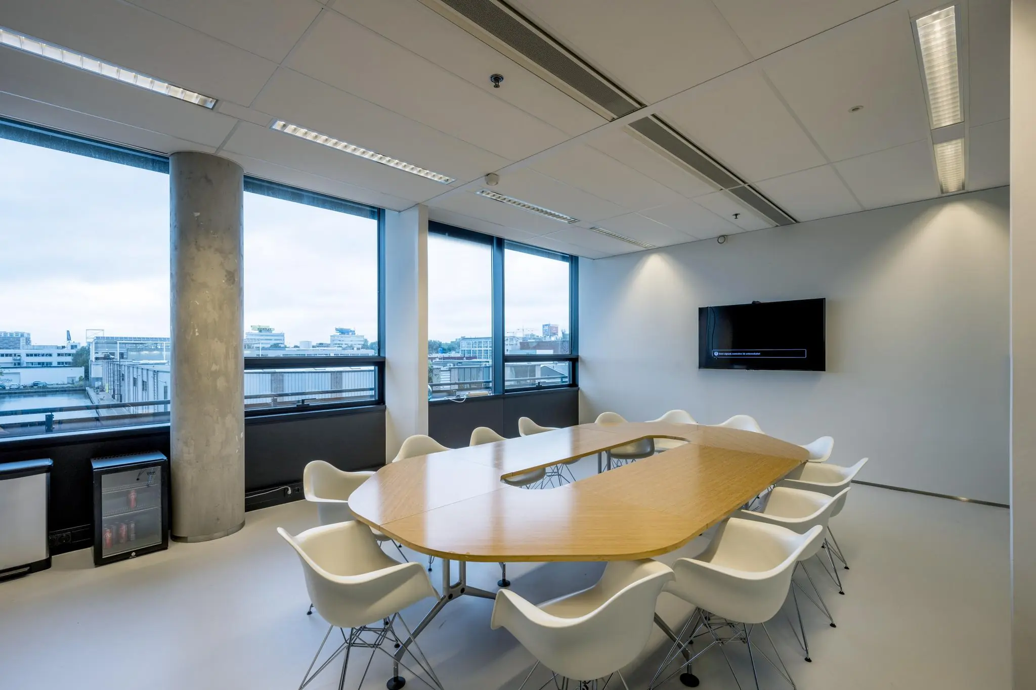 Vergaderruimte aan de Generaal Vetterstraat met een ovale houten tafel, witte stoelen en grote ramen met uitzicht op de stad.