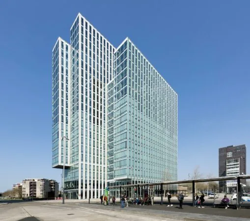 Hoog modern kantoorgebouw aan het Mandelaplein met een bushalte op de voorgrond.