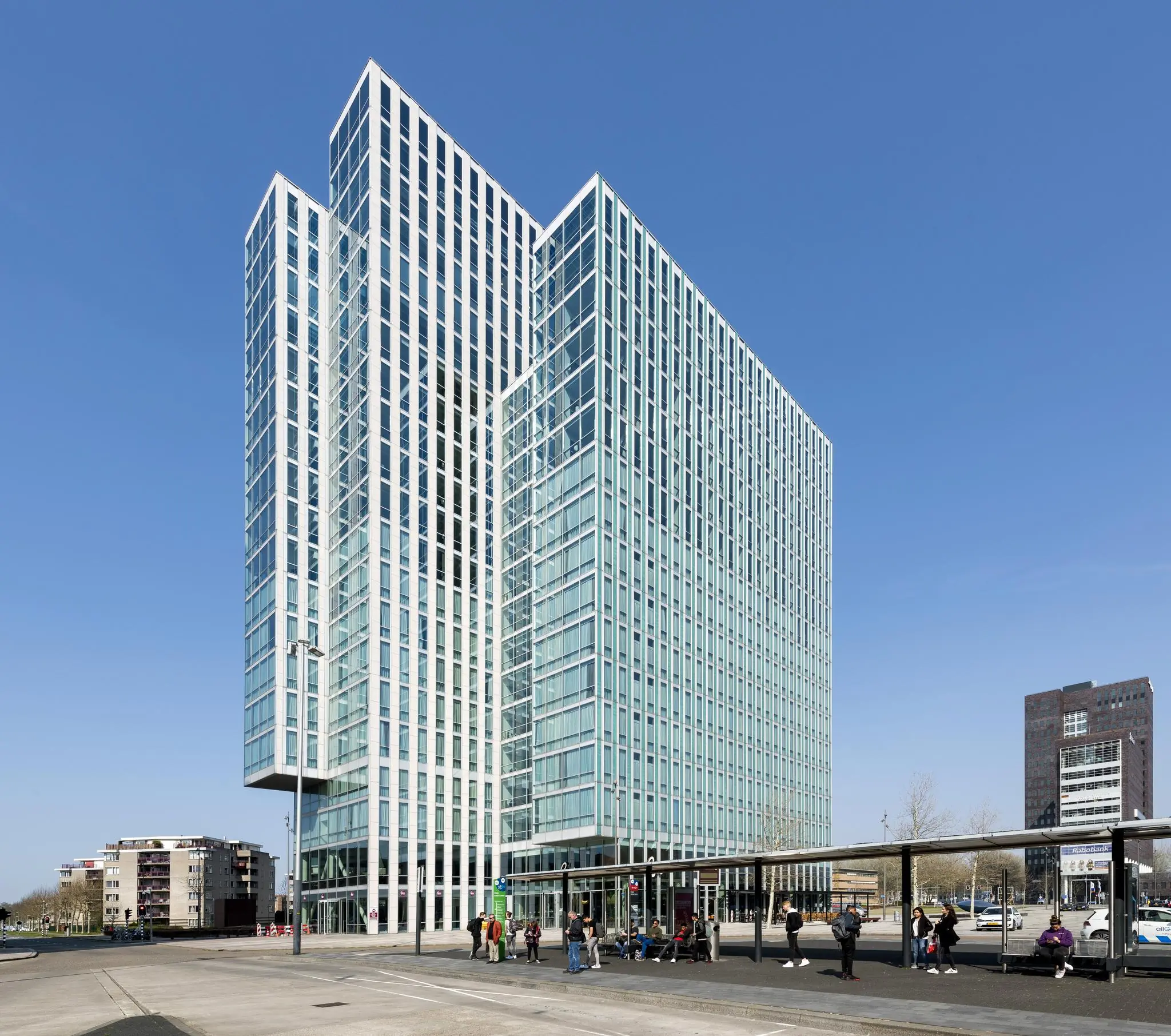 Hoog modern kantoorgebouw aan het Mandelaplein met een bushalte op de voorgrond.