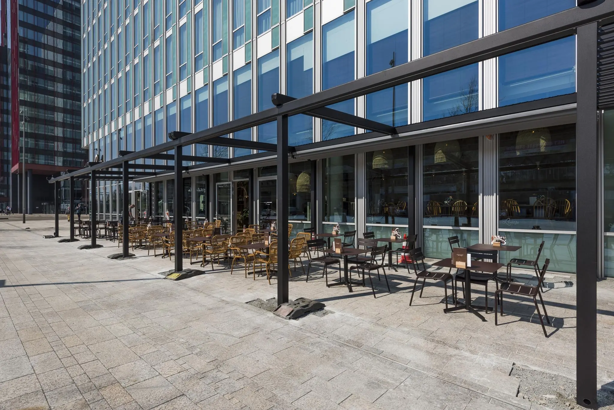 Terras met tafels en stoelen naast een modern kantoorgebouw aan het Mandelaplein.