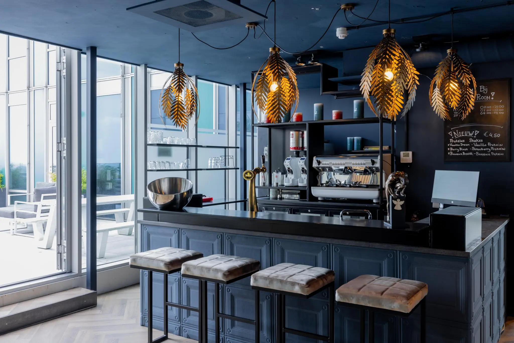 Moderne koffiebalie op het Mandelaplein met sfeervolle verlichting, barkrukken en uitzicht op een zonnig terras.