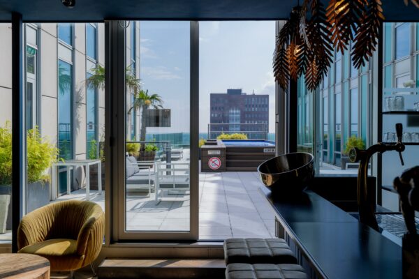 Luxe dakterras aan het Mandelaplein met zithoek, palmbomen en een klein zwembad, gezien vanuit een modern interieur met bar.