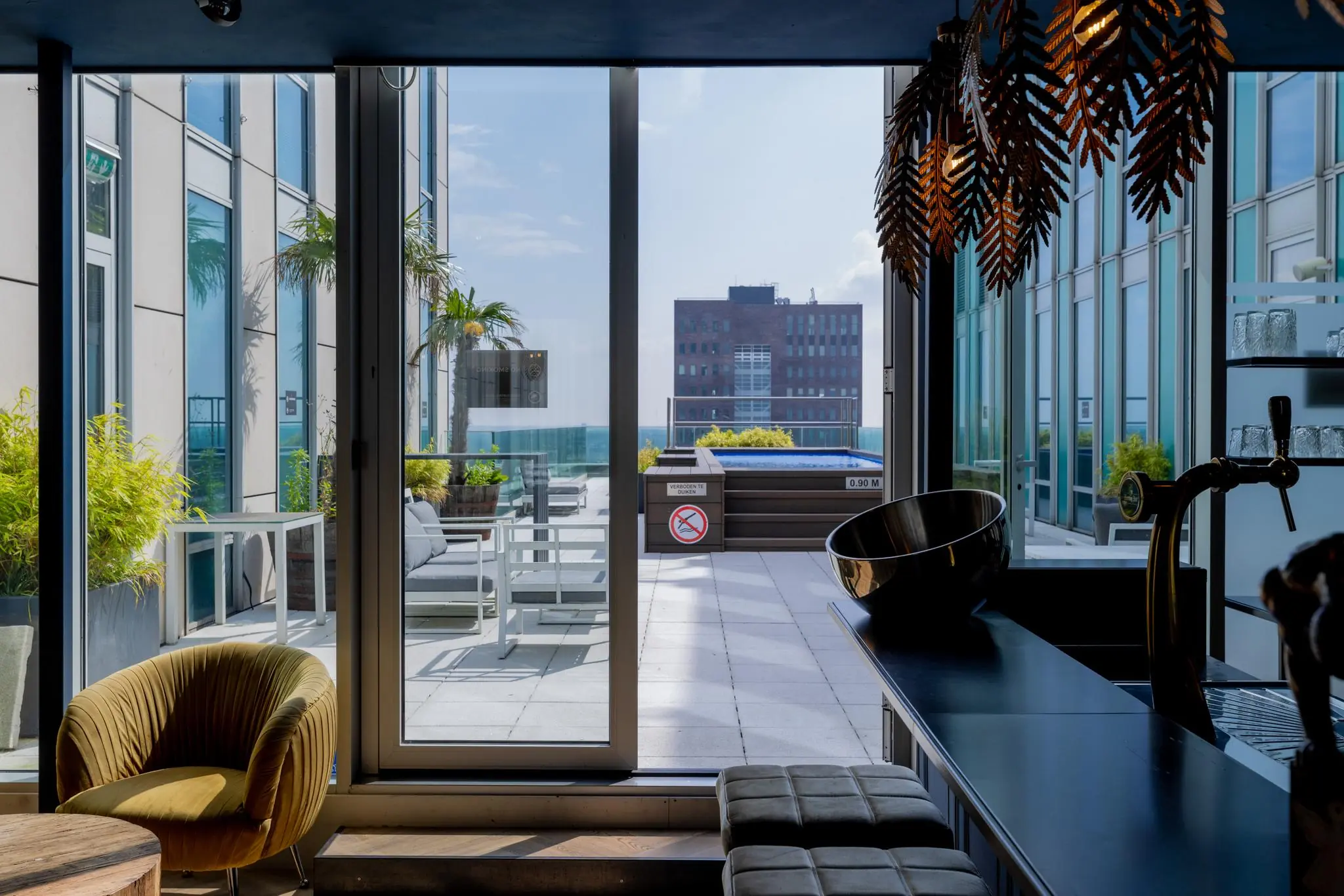 Luxe dakterras aan het Mandelaplein met zithoek, palmbomen en een klein zwembad, gezien vanuit een modern interieur met bar.