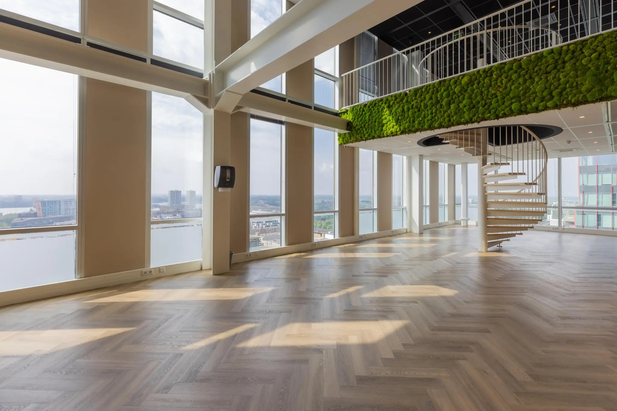 Lichte, moderne kantoorruimte aan het Mandelaplein met grote ramen, een wenteltrap en een groene moswand.