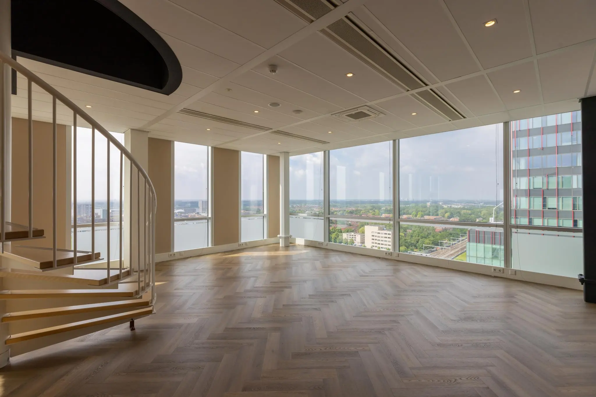 Lichte, lege ruimte met visgraatvloer, wenteltrap en panoramisch uitzicht op de stad vanaf het Mandelaplein.