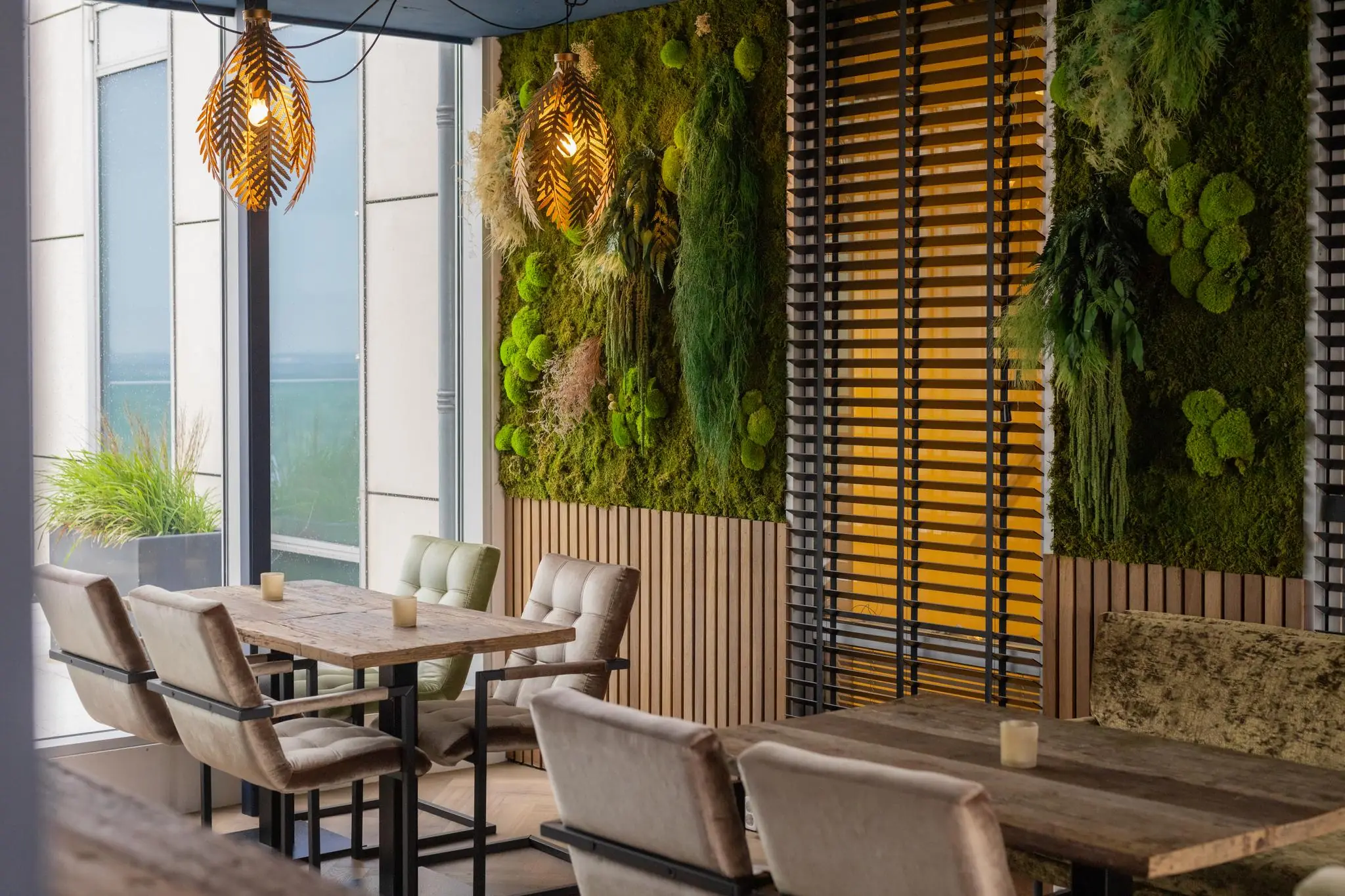 Modern ingericht restaurant aan het Mandelaplein met houten tafels, groene moswanden en sfeervolle verlichting.