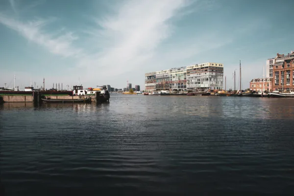 Uitzicht over het water op de Houthavens in Amsterdam met het moderne HNK-gebouw op de achtergrond en aangemeerde boten op de voorgrond.