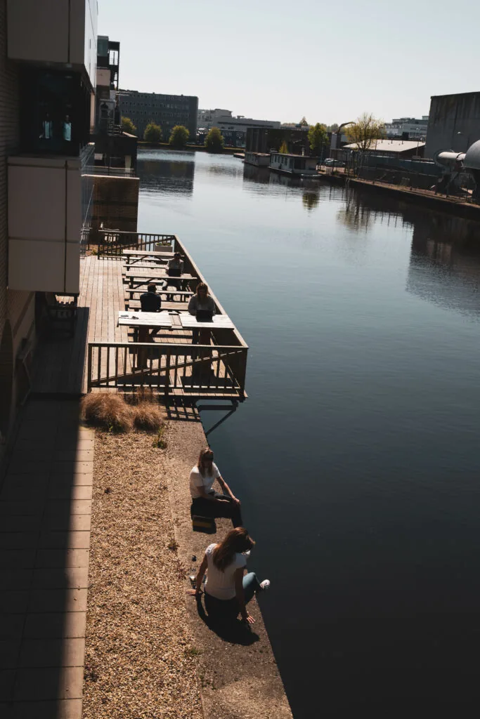 Mensen zitten en werken buiten aan het water bij HNK Amsterdam Schinkel.