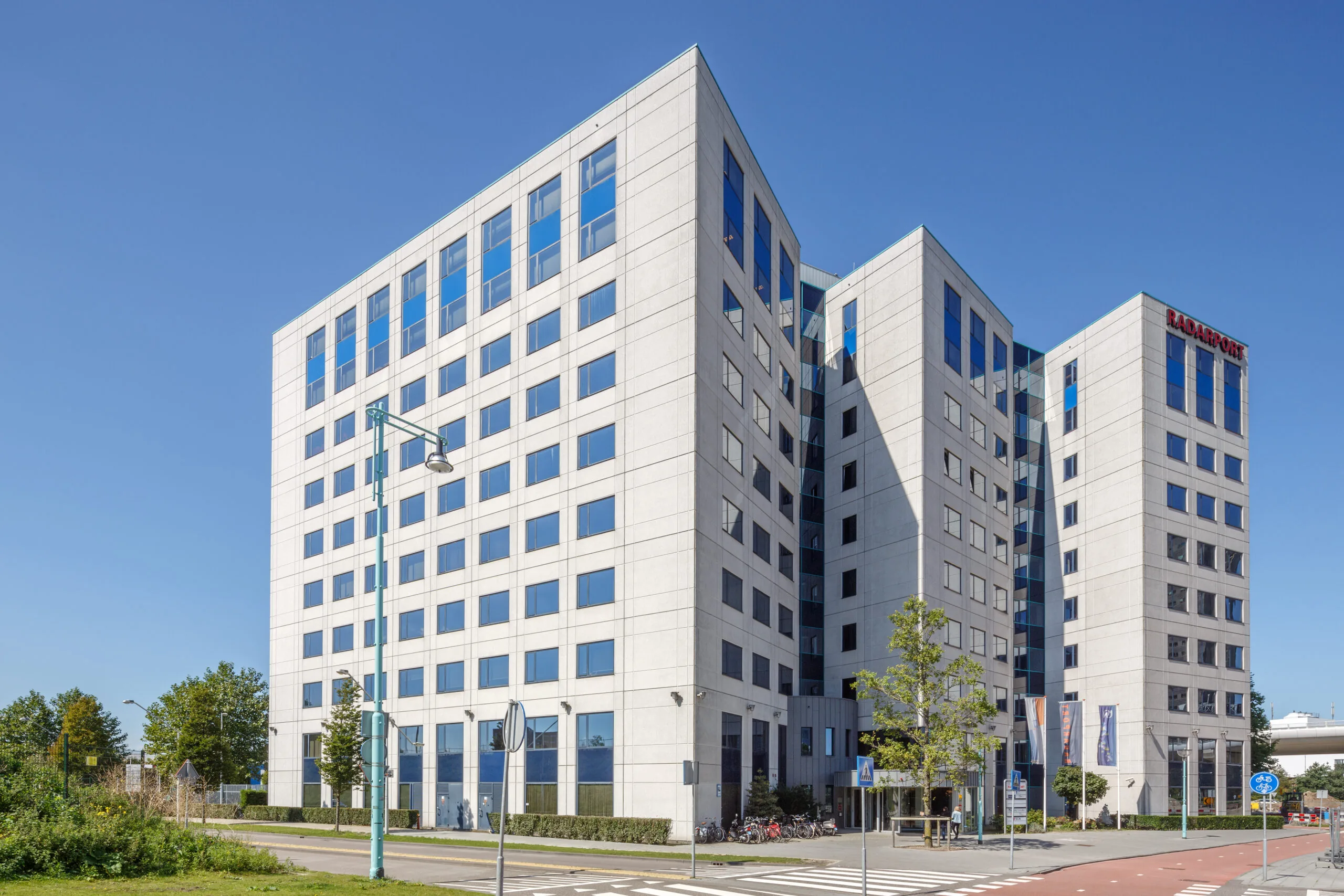 Kantoorgebouw HNK Amsterdam Sloterdijk met moderne gevel en opvallende glaspartijen tegen een strakblauwe lucht.