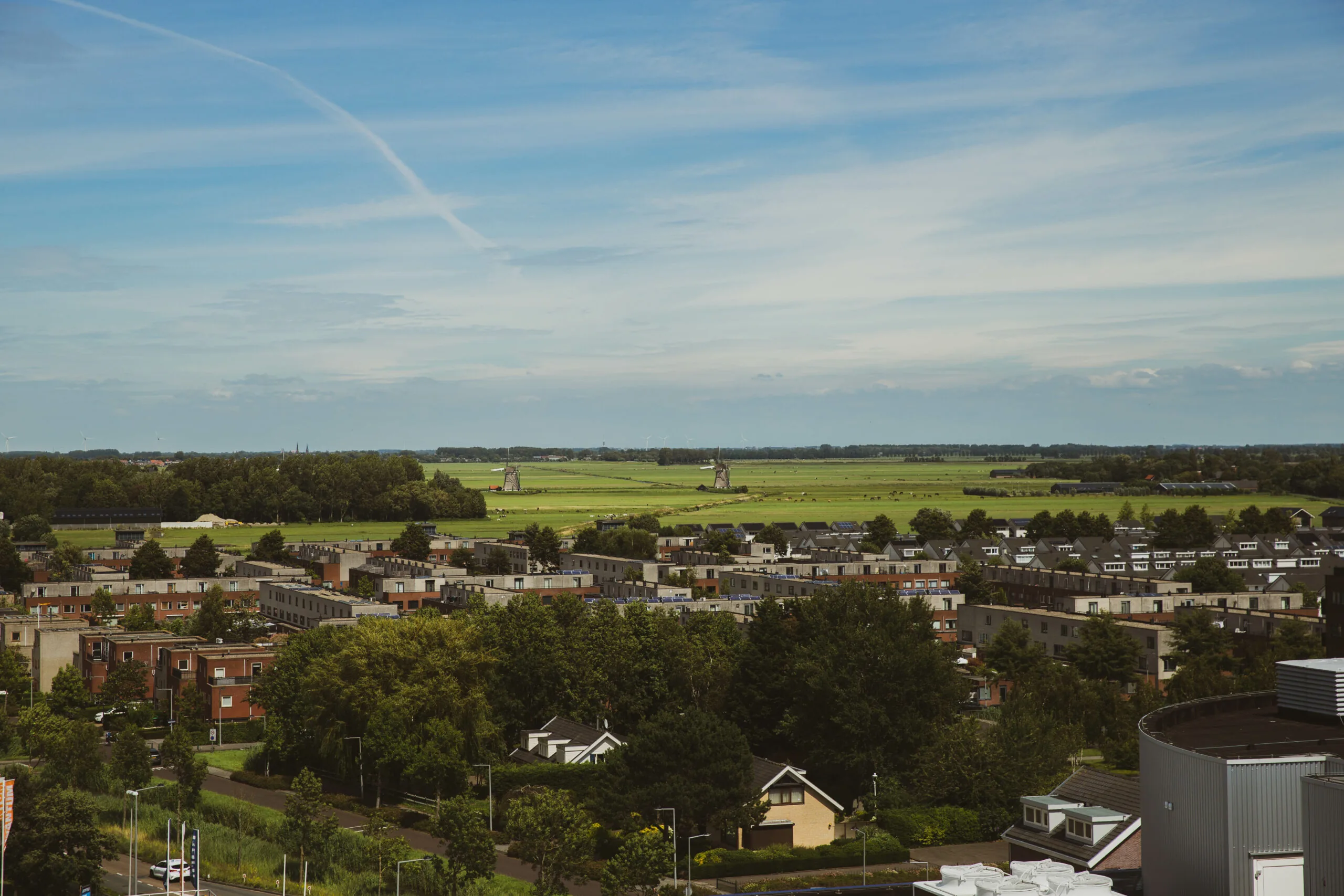 Uitzicht vanaf HNK Den Haag op een woonwijk met op de achtergrond groene velden en twee traditionele windmolens.