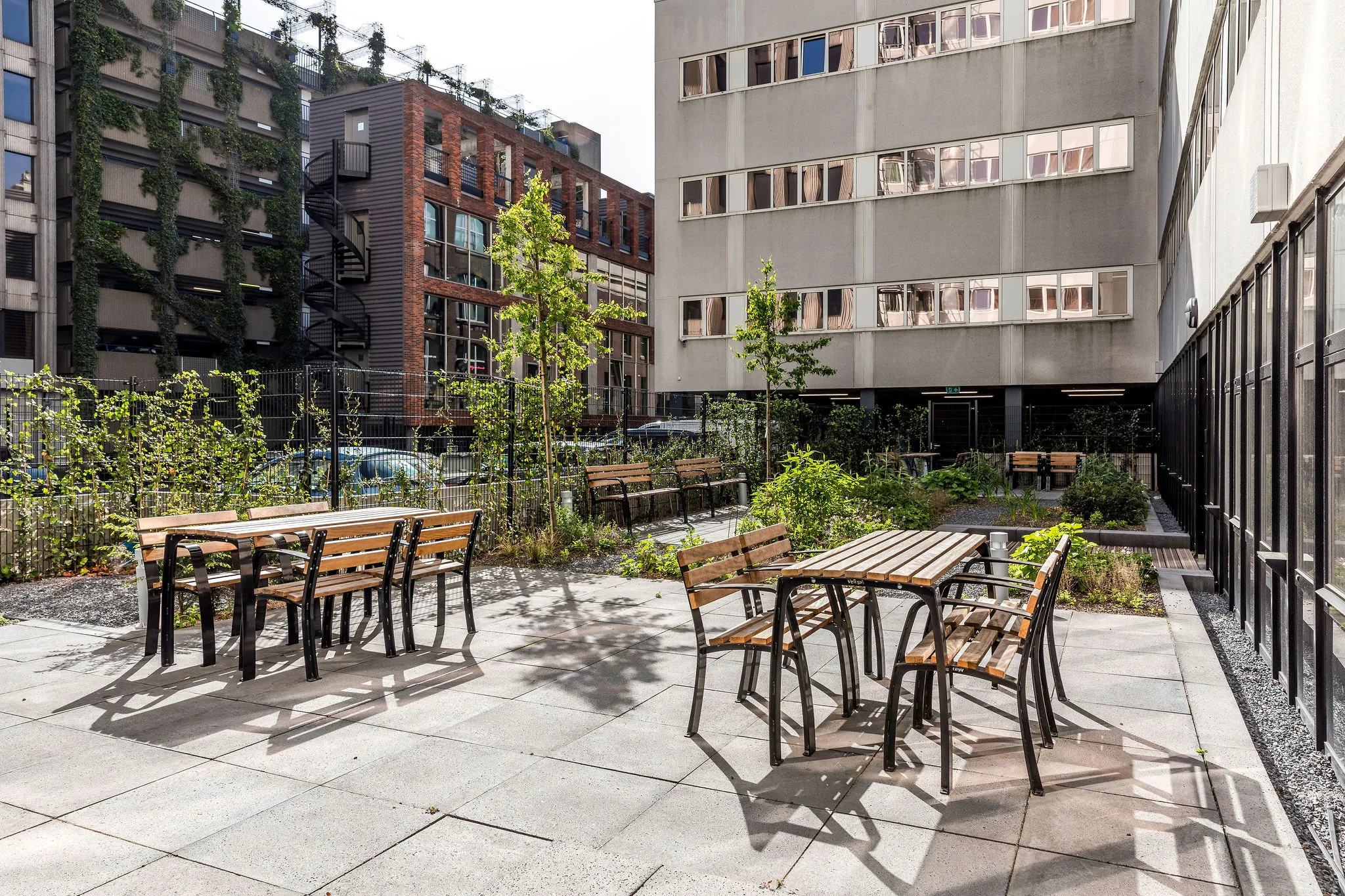 Buitenterras met houten zitbanken en tafels tussen kantoorgebouwen bij HNK Rotterdam Centrum.