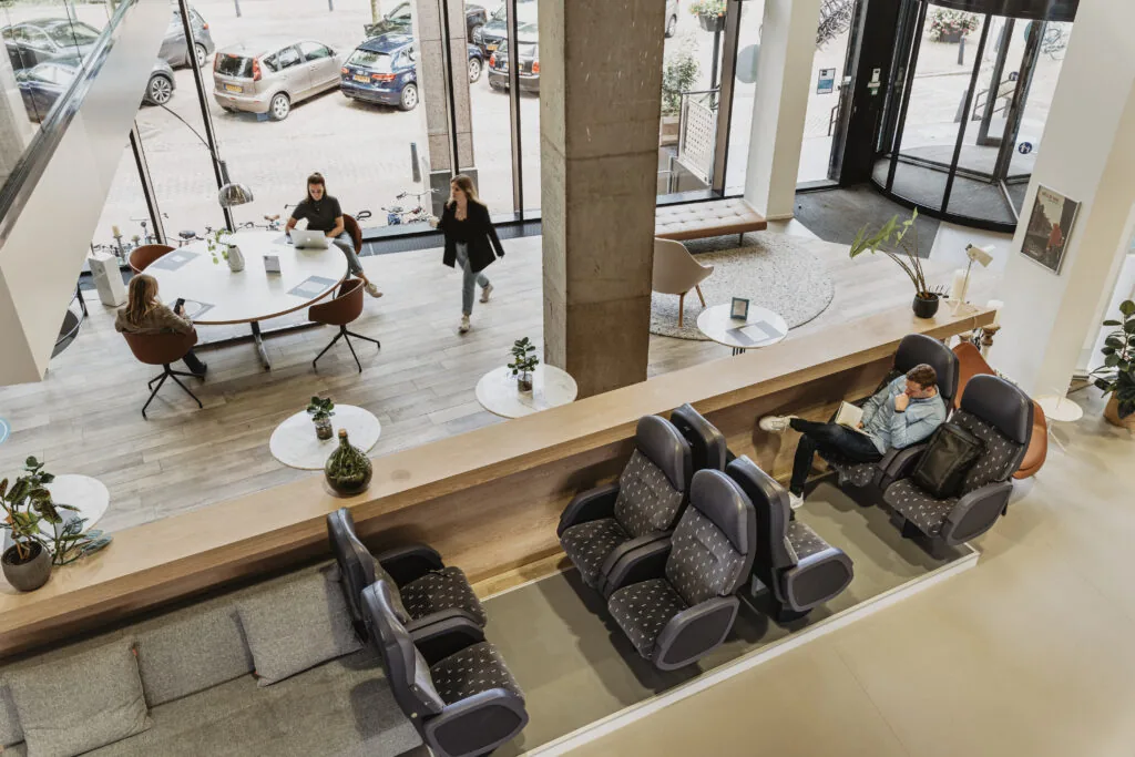 Moderne lobby van HNK Utrecht CS met werkplekken, loungezitplaatsen en mensen die aan het werk zijn of ontspannen.