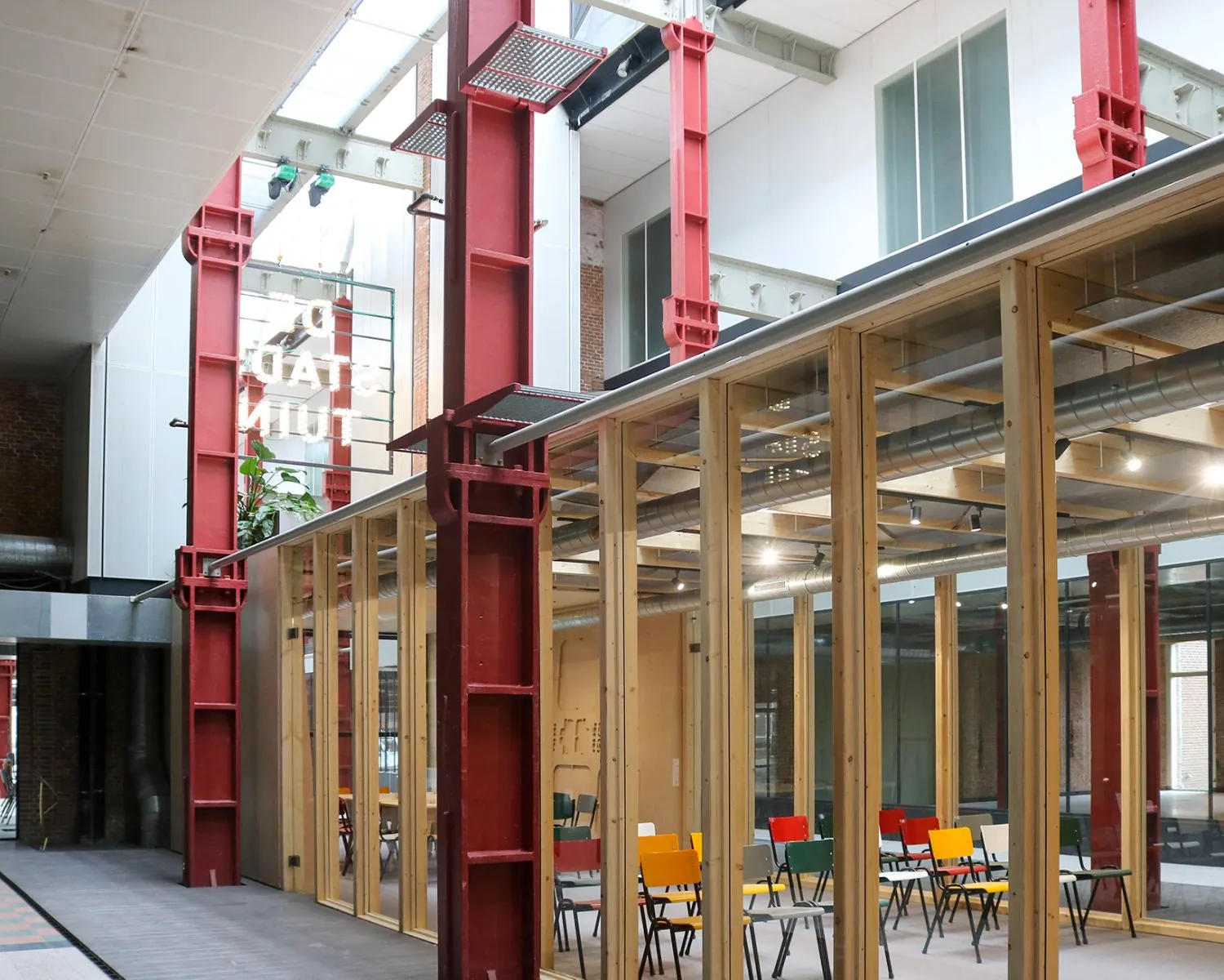 Moderne kantoorruimte met glazen wanden, kleurrijke stoelen en rode stalen balken in verzamelgebouw De Stadstuin aan de Vijf Werelddelen 69 in Rotterdam.
