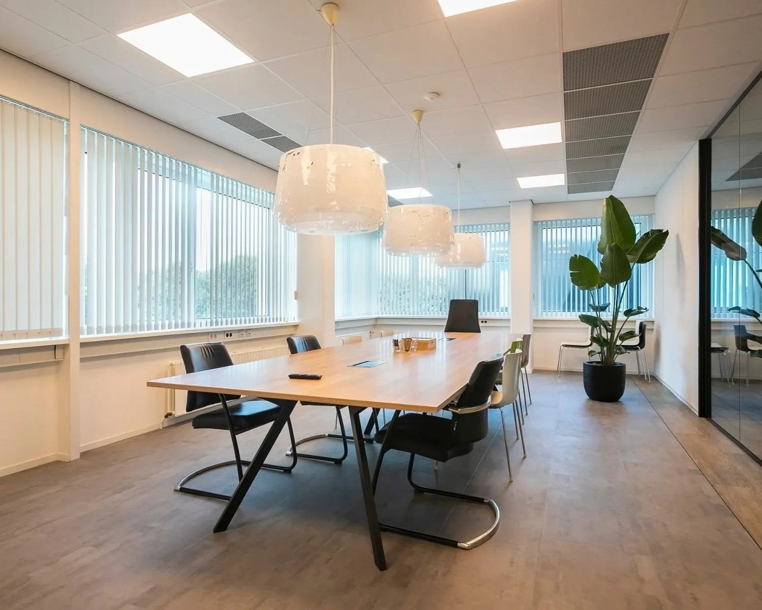 Moderne vergaderruimte in een kantoor aan de Bolderweg 2a in Almere met een lange houten tafel, designstoelen, hanglampen en grote raampartijen met lamellen.