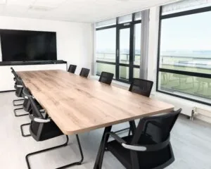 Moderne vergaderruimte met lange houten tafel, zwarte stoelen en groot scherm in een kantoor aan de Pascallaan 60-78 in Lelystad.