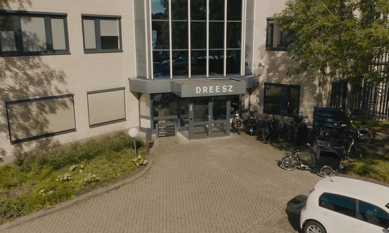 Vooraanzicht van het kantoorgebouw van Dreesz met fietsen en een auto voor de ingang.
