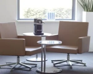 Zithoek met twee bruine bureaustoelen, een koffietafel en een koffiezetapparaat in een kantoorruimte aan de Arlandaweg 92 in Amsterdam.