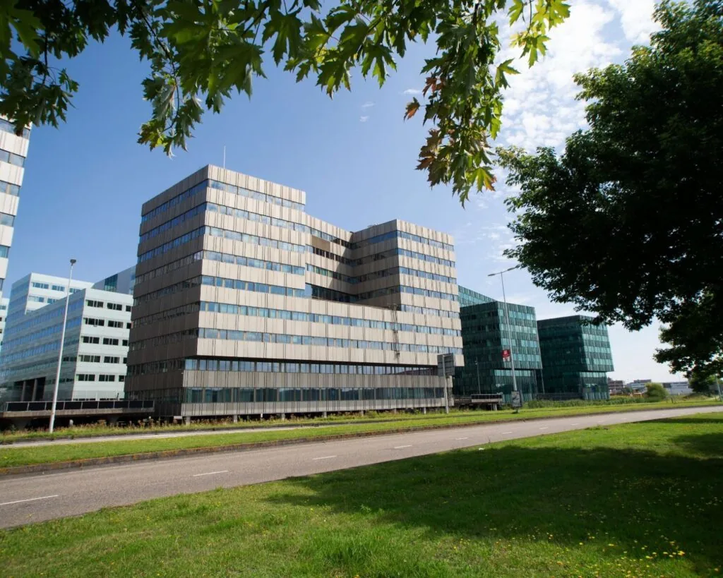 Modern kantoorgebouw aan de Herikerbergweg 288-290 in Amsterdam, gezien vanaf de straat met groen en bomen op de voorgrond.