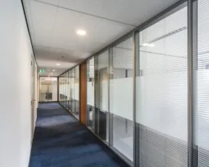 Lichte kantoorhal met glazen wanden en blauwe vloerbedekking in het kantoorgebouw aan de Kronenburgsingel 525 in Arnhem.