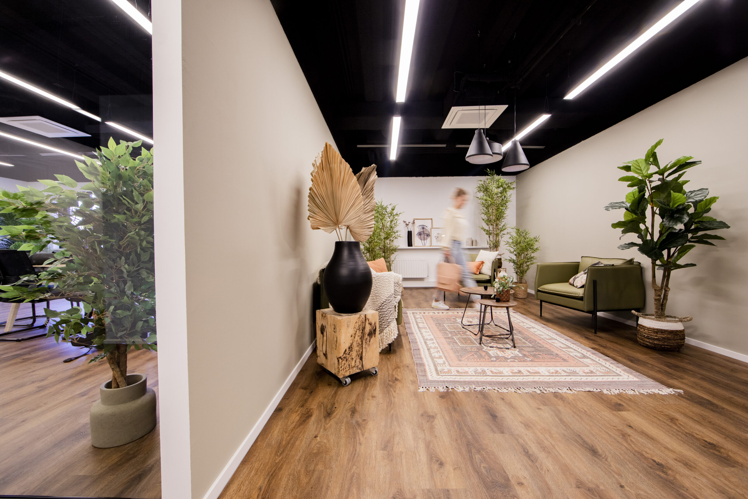 Een moderne kantoorruimte met planten, lounge stoelen en een wandkleed op de vloer.