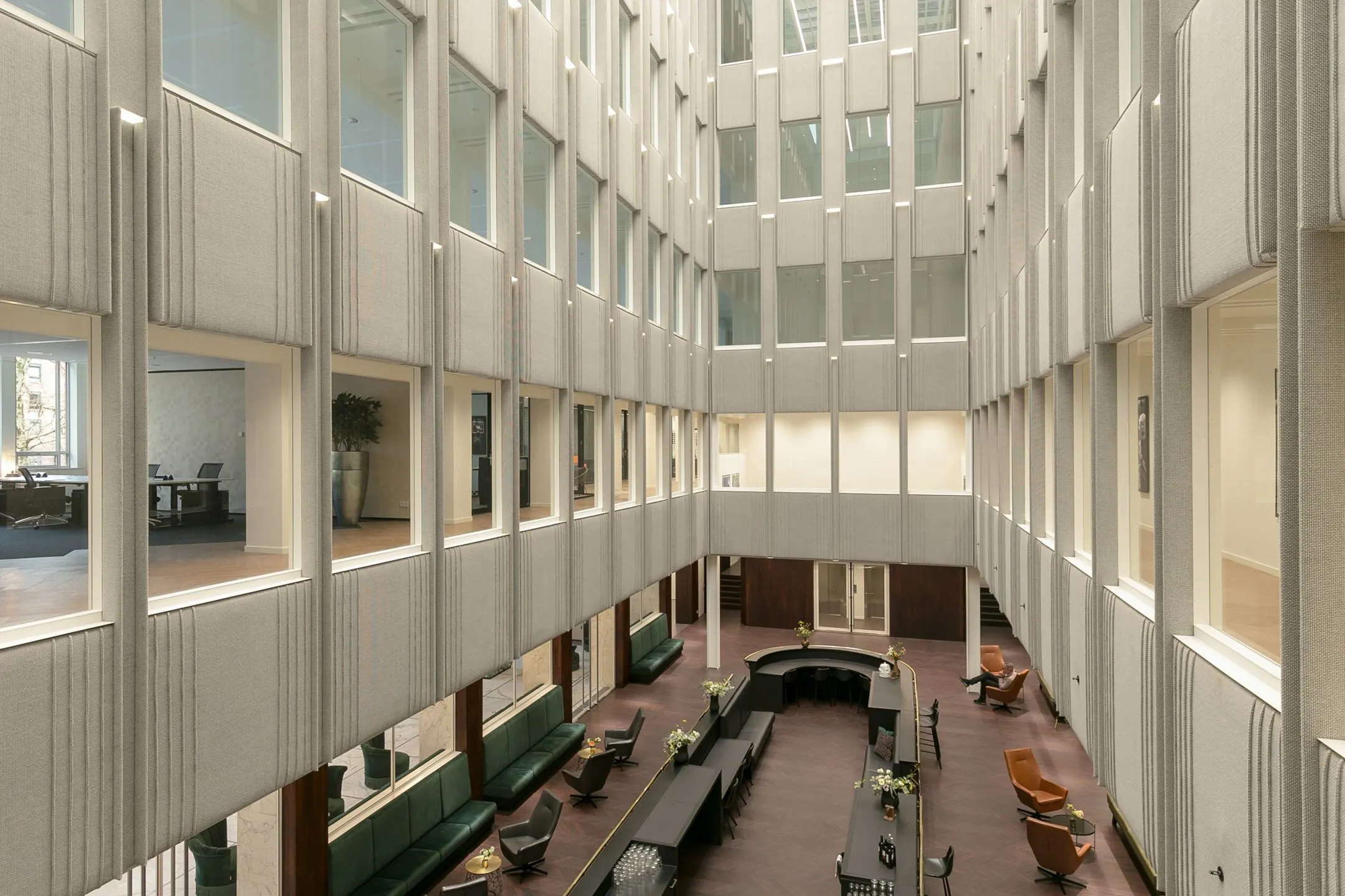 Moderne, open binnenruimte van een kantoorgebouw met zitgedeelte en bureau’s aan de zijkanten van de verdiepingen.