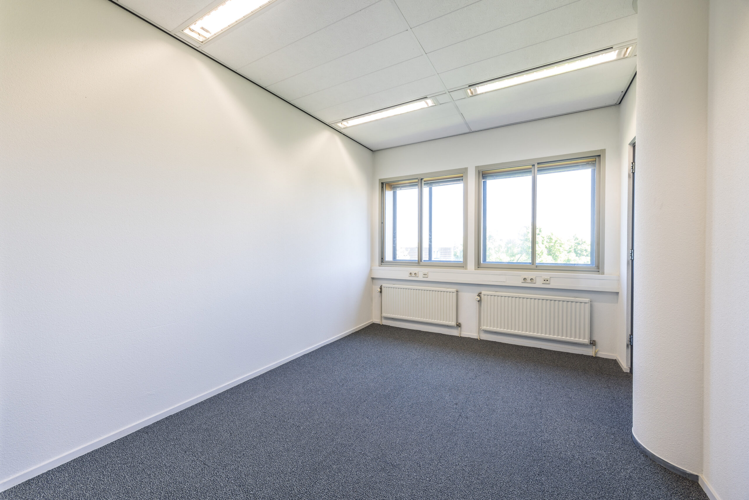 Leeg en licht kantoor met drie ramen, grijze vloerbedekking en witte muren in Element Offices, Utrecht.