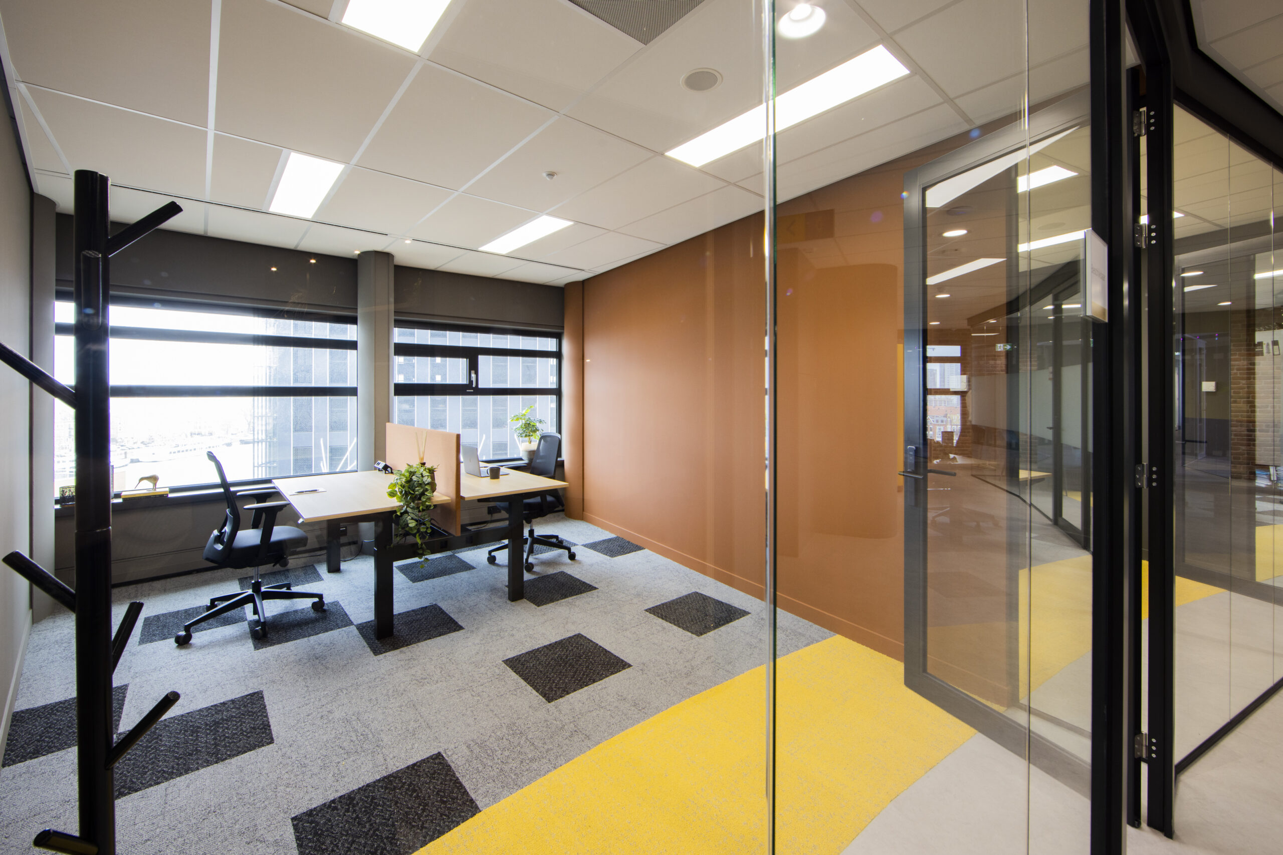 Moderne kantoorruimte in Rotterdam met glazen wanden, bureaus en planten.
