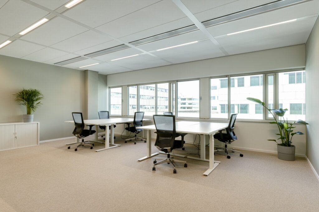 Moderne kantoorruimte met vier bureaus, bureaustoelen en natuurlijke lichtinval.