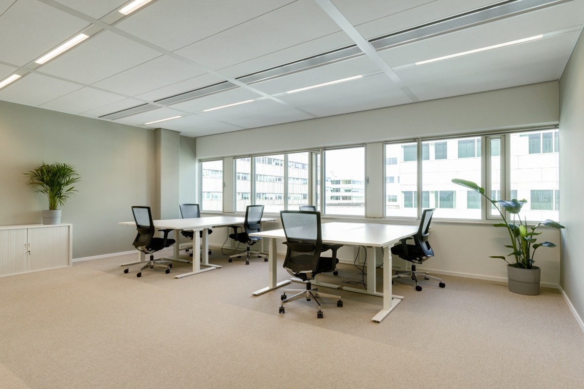 Moderne kantoorruimte met vier bureaus, bureaustoelen en natuurlijke lichtinval.