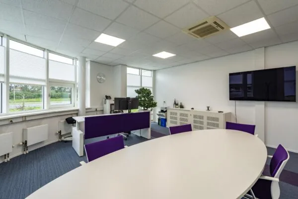 Moderne kantoorruimte aan het Rhijnspoor met vergadertafel, werkplekken, en een flatscreen tegen een witte muur.