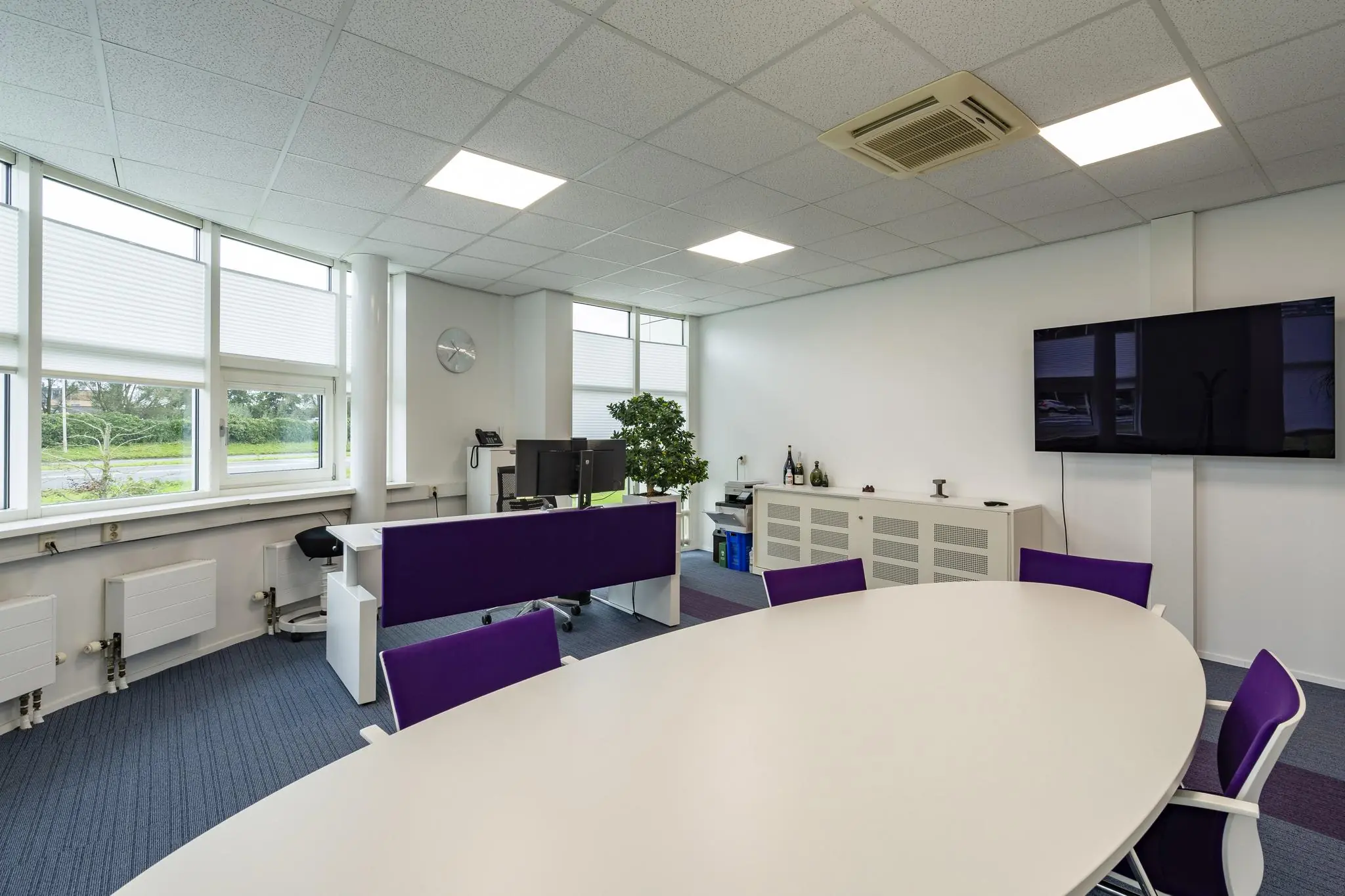 Moderne kantoorruimte aan het Rhijnspoor met vergadertafel, werkplekken, en een flatscreen tegen een witte muur.