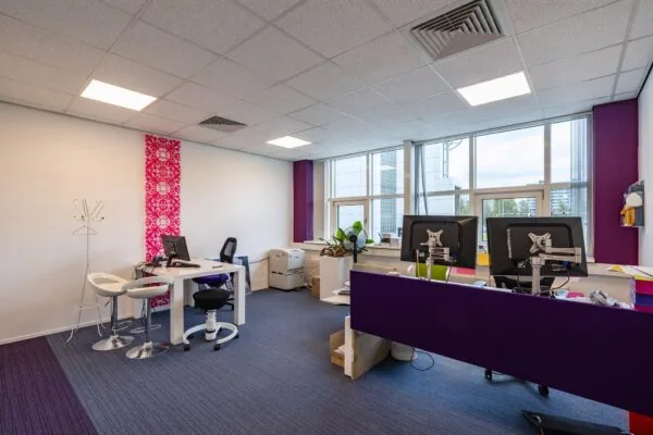 Modern kantoorinterieur in het Rhijnspoor-gebouw met werkplekken, paarse accenten en grote ramen.